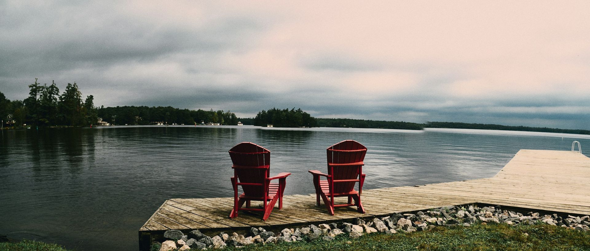 Two red Muskoka chairs on a lake dock